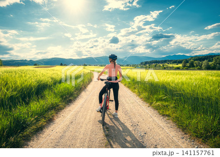 Woman riding mountain bike on dirt road and green wheat fields Woman riding mountain bike on dirt road and green wheat fields 141157761