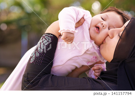 Muslim mother, outdoor and kiss baby for care, connection and bonding together in summer. Mom, kid and love on cheek for infant, adorable child and Islamic family at garden for healthy relationship Muslim mother, outdoor and kiss baby for care, connection and bonding together in summer. Mom, kid and love on cheek for infant, adorable child and Islamic family at garden for healthy relationship 141157794