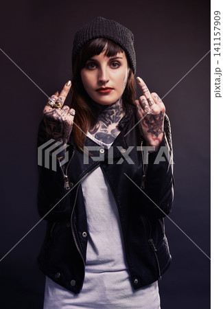 Portrait, fashion woman with middle finger, tattoo or attitude in studio with gothic, style or artistic expression on black background. Rebel, face and emo model with hand, emoji or grunge aesthetic Portrait, fashion woman with middle finger, tattoo or attitude in studio with gothic, style or artistic expression on black background. Rebel, face and emo model with hand, emoji or grunge aesthetic 141157909