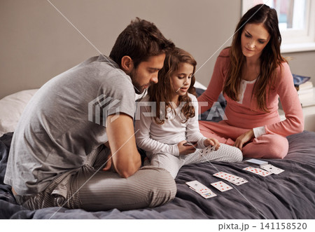 Parents, girl and playing cards to relax in home with bonding, learning and fun with strategy in bedroom. Father, mother and daughter with games, maths and teaching with connection in family house Parents, girl and playing cards to relax in home with bonding, learning and fun with strategy in bedroom. Father, mother and daughter with games, maths and teaching with connection in family house 141158520