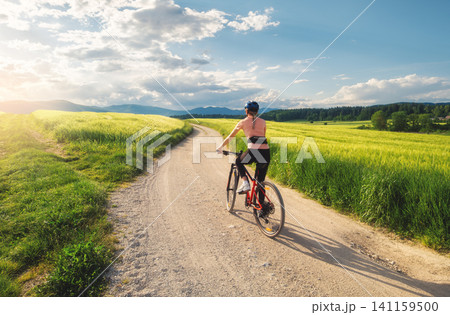 Woman riding mountain bike on dirt road and green wheat fields Woman riding mountain bike on dirt road and green wheat fields 141159500