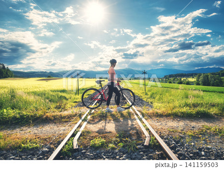Female cyclist riding mountain bike and rural railroad at sunset Female cyclist riding mountain bike and rural railroad at sunset 141159503