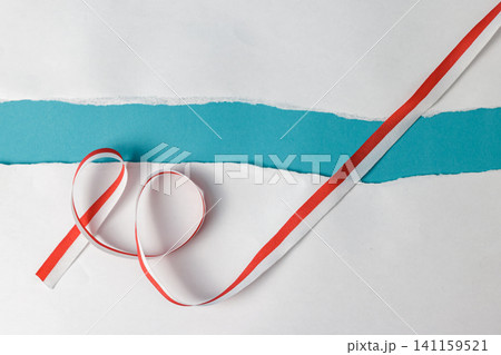 Elegant red and white curled ribbon laid across a white surface with a torn paper edge revealing a vibrant turquoise or teal blue background. High Quality Photo Elegant red and white curled ribbon laid across a white surface with a torn paper edge revealing a vibrant turquoise or teal blue background. High Quality Photo 141159521