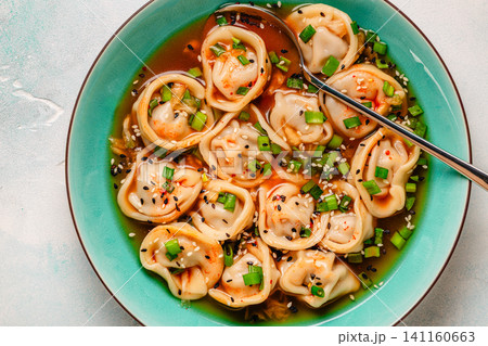 Dumplings served in a bowl with broth and green onions. 141160663