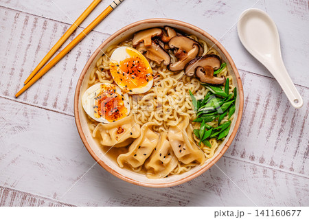 Bowl of noodles with dumplings, egg, and mushrooms on a wooden table Bowl of noodles with dumplings, egg, and mushrooms on a wooden table 141160677