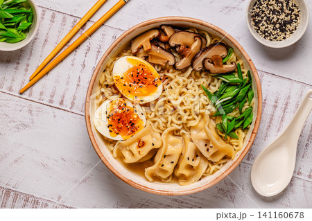 Bowl of noodles with dumplings, egg, and mushrooms on a wooden table 141160678
