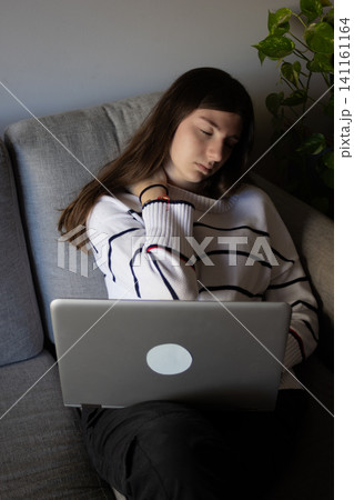 Young woman feeling exhausted and stressed while working remotely from home on a laptop, experiencing neck pain and frustration from long hours and deadlines 141161164