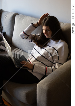 Young woman working remotely from home on a laptop, feeling stressed and frustrated with a deadline, experiencing tiredness and displeasure while concentrating on work tasks Young woman working remotely from home on a laptop, feeling stressed and frustrated with a deadline, experiencing tiredness and displeasure while concentrating on work tasks 141161176