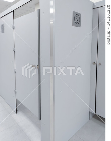 Accessible restroom stalls with white partitions and signage indicating facilities for individuals with disabilities in a modern public restroom environment Accessible restroom stalls with white partitions and signage indicating facilities for individuals with disabilities in a modern public restroom environment 141161220