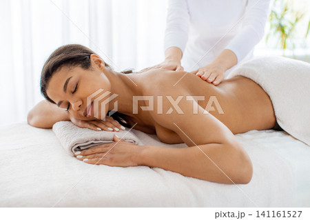 Black woman resting on towels while receiving back massage from spa therapist Black woman resting on towels while receiving back massage from spa therapist 141161527