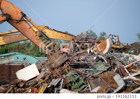 Excavator magnet lifting steel scraps from recycling materials pile at scrap yard in recycling factory. Excavator with electro and magnetic sucker magnet chuck. Special excavator. Scrap metal magnet. Excavator magnet lifting steel scraps from recycling materials pile at scrap yard in recycling factory. Excavator with electro and magnetic sucker magnet chuck. Special excavator. Scrap metal magnet. 141162153
