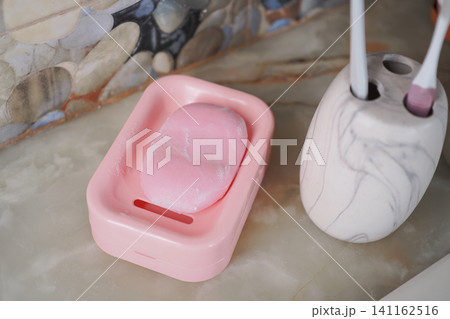 Pink soap on a dish beside a toothbrush holder Pink soap on a dish beside a toothbrush holder 141162516