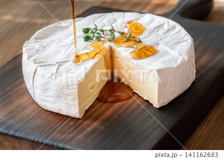 Golden Maple Syrup Pouring Over Camembert Cheese On Rustic Wooden Board Elegantly Golden Maple Syrup Pouring Over Camembert Cheese On Rustic Wooden Board Elegantly 141162683