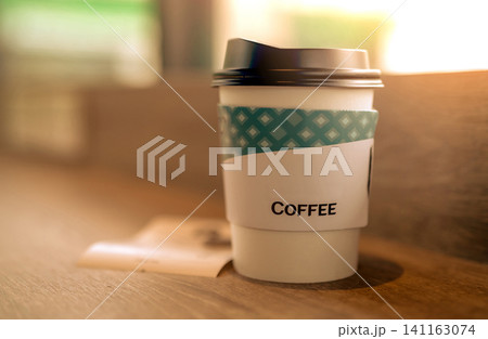 Paper coffee glass in coffee shop on brown wooden table at coffee cafe in the morning with sunlight. Latte, cappuccino, or espresso in paper glass. Disposable paper cup. Green packaging. Hot drink. Paper coffee glass in coffee shop on brown wooden table at coffee cafe in the morning with sunlight. Latte, cappuccino, or espresso in paper glass. Disposable paper cup. Green packaging. Hot drink. 141163074