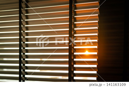 Opened venetian plastic blinds with morning sunlight streaming through a residential window. Modern living room design, privacy. Horizontal slatted shades, minimalist interior design, privacy control. Opened venetian plastic blinds with morning sunlight streaming through a residential window. Modern living room design, privacy. Horizontal slatted shades, minimalist interior design, privacy control. 141163109
