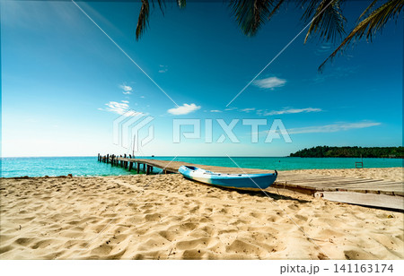 Beautiful view tropical paradise beach of resort. Coconut tree, wooden bridge, and kayak at resort on sunny day. Summer vacation concept. Summer vibes. Golden sand beach of resort with blue sky. Beautiful view tropical paradise beach of resort. Coconut tree, wooden bridge, and kayak at resort on sunny day. Summer vacation concept. Summer vibes. Golden sand beach of resort with blue sky. 141163174
