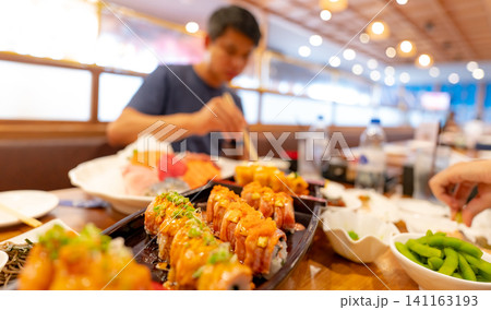 Selective focus on Japanese food in a Japanese restaurant. Salmon sushi on a plate with blurred man eating Japanese food with chopsticks in the restaurant. Healthy Asian food. Salmon sushi menu. Selective focus on Japanese food in a Japanese restaurant. Salmon sushi on a plate with blurred man eating Japanese food with chopsticks in the restaurant. Healthy Asian food. Salmon sushi menu. 141163193