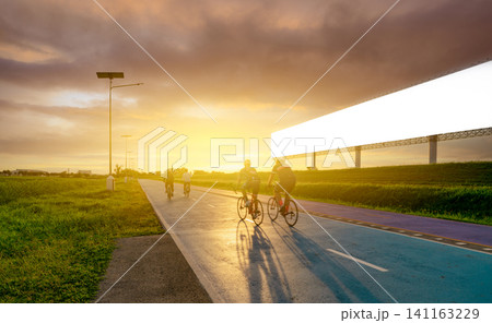 Sports man ride bicycles on the road in the evening near blank advertising billboard with sunset sky. Summer outdoor exercise for healthy and happy life. Cyclist riding mountain bike on bike lane. Sports man ride bicycles on the road in the evening near blank advertising billboard with sunset sky. Summer outdoor exercise for healthy and happy life. Cyclist riding mountain bike on bike lane. 141163229