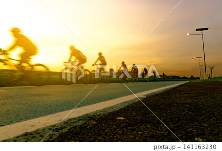 Blur photo sports man ride bicycles with speed motion on the road in the evening with sunset sky. Summer outdoor exercise for healthy and happy life. Cyclist riding mountain bike on bike lane. Team. Blur photo sports man ride bicycles with speed motion on the road in the evening with sunset sky. Summer outdoor exercise for healthy and happy life. Cyclist riding mountain bike on bike lane. Team. 141163230