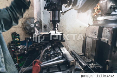 Selective focus on milling machine. Blurred worker is working on milling machine to milling metal plate. Tool for cut metal workpiece. Steel manufacturing factory. Milling process. Machine in workshop Selective focus on milling machine. Blurred worker is working on milling machine to milling metal plate. Tool for cut metal workpiece. Steel manufacturing factory. Milling process. Machine in workshop 141163232