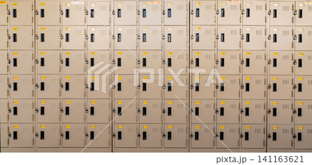 Closeup beige locker with lock and numbered yellow tags at locker room. Locker for safety and security storage. Row of locker with locked door background. 141163621