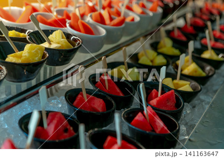 Selective focus tropical fruit buffet at event in restaurant. Catering food. Fresh watermelon and pineapple slices in small bowl on crushed ice on luxury table. Banquet service. Fruit buffet catering. Selective focus tropical fruit buffet at event in restaurant. Catering food. Fresh watermelon and pineapple slices in small bowl on crushed ice on luxury table. Banquet service. Fruit buffet catering. 141163647
