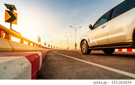 Curve concrete road with curve traffic sign and red-white prohibited stop sign. Solar panel energy on curve traffic sign. Road trip. Motion blur of white car driving on the road. Road trip on summer. Curve concrete road with curve traffic sign and red-white prohibited stop sign. Solar panel energy on curve traffic sign. Road trip. Motion blur of white car driving on the road. Road trip on summer. 141163834