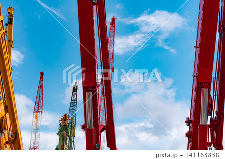 Crawler crane against blue sky and white clouds. Real estate industry. Red crawler crane use reel lift up equipment in construction site. Crane for rent. Crane dealership for construction business. Crawler crane against blue sky and white clouds. Real estate industry. Red crawler crane use reel lift up equipment in construction site. Crane for rent. Crane dealership for construction business. 141163838