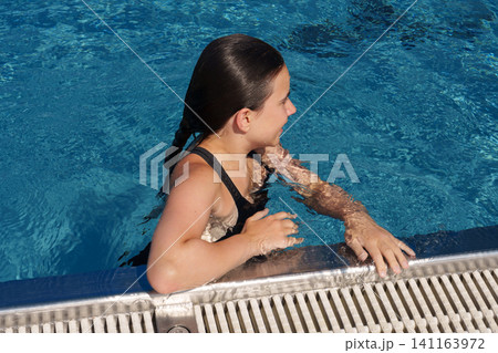 Teen girl holding pool edge after swimming in outdoor pool 141163972