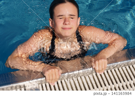 Teen girl catching breath at pool edge after swimming practice 141163984