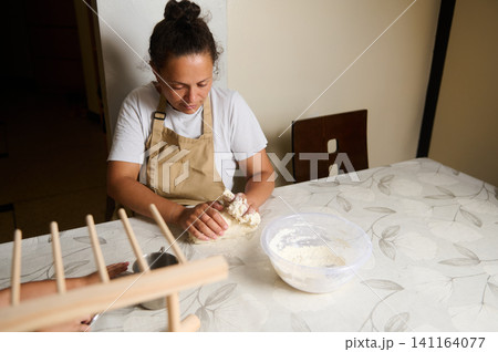 Woman kneading dough at kitchen table preparing homemade bread 141164077