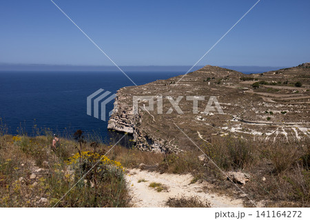 Beautiful scenic view of a rocky coast and cliff cape ending in the blue sea in Malta. Beautiful scenic view of a rocky coast and cliff cape ending in the blue sea in Malta. 141164272