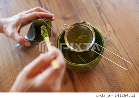 Sifting matcha powder into bowl for homemade iced latte recipe Sifting matcha powder into bowl for homemade iced latte recipe 141164312