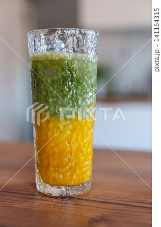 Layered iced mango matcha latte in tall glass on kitchen table Layered iced mango matcha latte in tall glass on kitchen table 141164315