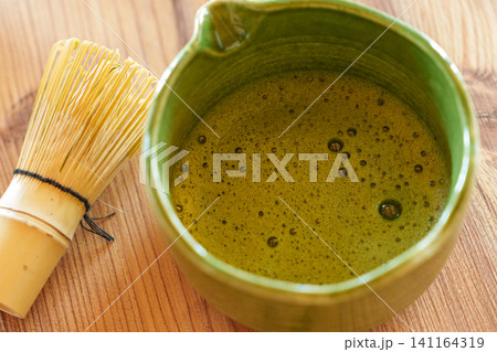 Fresh whisked matcha in ceramic bowl with bamboo whisk nearby Fresh whisked matcha in ceramic bowl with bamboo whisk nearby 141164319