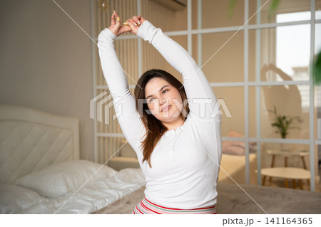 Woman stretching arms in cozy bedroom during a serene morning routine. Wellness and calming bedroom lifestyle with focus on waking up habits Woman stretching arms in cozy bedroom during a serene morning routine. Wellness and calming bedroom lifestyle with focus on waking up habits 141164365
