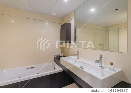 Contemporary bathroom interior with white built in bathtub, double sink vanity, large wall mirror, chrome fixtures, bright neutral finishes, spacious modern residential design 141164527