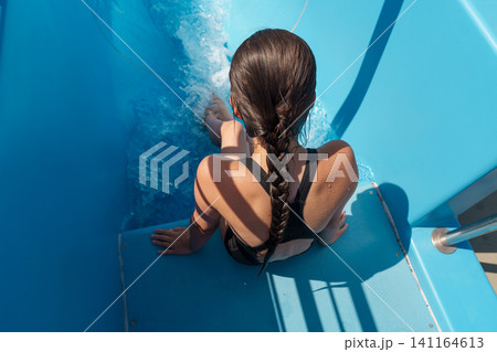 Teen girl sliding down blue water slide at outdoor pool in summer Teen girl sliding down blue water slide at outdoor pool in summer 141164613
