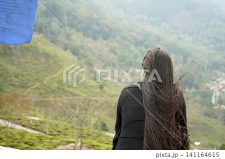 Young woman with long hair looking out over a scenic tea plantation landscape Young woman with long hair looking out over a scenic tea plantation landscape 141164615