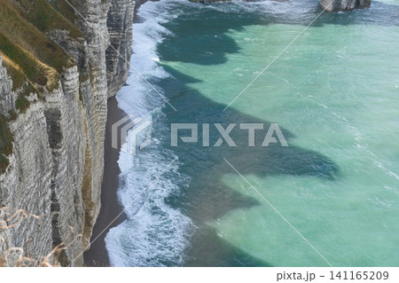 Chalk cliffs at Alabaster Coast. Etretat, France. Ocean view landscape with turquoise water and waves with foam, tourism and traveling to Normandy Chalk cliffs at Alabaster Coast. Etretat, France. Ocean view landscape with turquoise water and waves with foam, tourism and traveling to Normandy 141165209