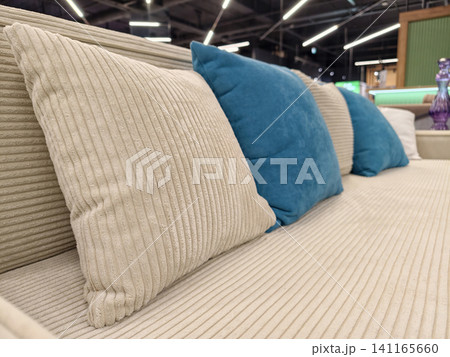 A modern beige sofa with a mix of beige and blue cushions, available for sale in a furniture store A modern beige sofa with a mix of beige and blue cushions, available for sale in a furniture store 141165660