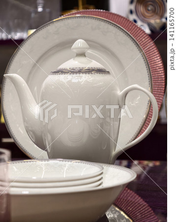 White porcelain tableware set with teapot plates and salad bowls presented in luxury retail arrangement highlighting smooth ceramic finish and refined elegant design for premium kitchenware display White porcelain tableware set with teapot plates and salad bowls presented in luxury retail arrangement highlighting smooth ceramic finish and refined elegant design for premium kitchenware display 141165700