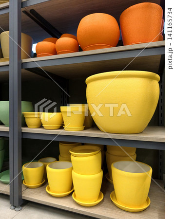 Yellow and red ceramic flower pots with saucers in large and small sizes displayed on shelves in a retail store garden section 141165734
