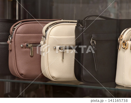 Assorted leather handbags in different colors displayed neatly behind a store window Assorted leather handbags in different colors displayed neatly behind a store window 141165738