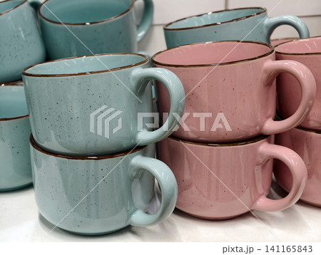 Blue and pink ceramic cups arranged on store shelves showing basic colorful tableware collection designed for everyday kitchen use and practical retail display Blue and pink ceramic cups arranged on store shelves showing basic colorful tableware collection designed for everyday kitchen use and practical retail display 141165843