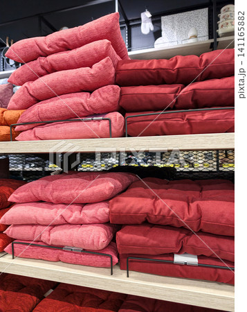 Red seat cushions displayed on supermarket shelves with neatly arranged soft chair pads and vibrant home textile comfort accessories in retail store interior Red seat cushions displayed on supermarket shelves with neatly arranged soft chair pads and vibrant home textile comfort accessories in retail store interior 141165882