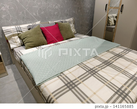 Room interior showing a bed, pillows, one red, a wardrobe, and a nightstand, with wallpaper on the walls, items displayed as samples for sale in a supermarket Room interior showing a bed, pillows, one red, a wardrobe, and a nightstand, with wallpaper on the walls, items displayed as samples for sale in a supermarket 141165885