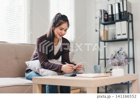 Asian woman using laptop, reviewing financial documents, managing bills and budgeting in cozy home. Asian woman using laptop, reviewing financial documents, managing bills and budgeting in cozy home. 141166552