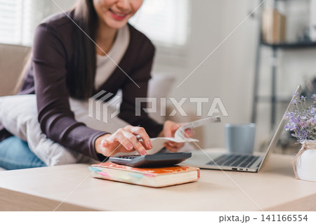 Close up of woman using calculator and holding receipts while managing finances at home. Close up of woman using calculator and holding receipts while managing finances at home. 141166554