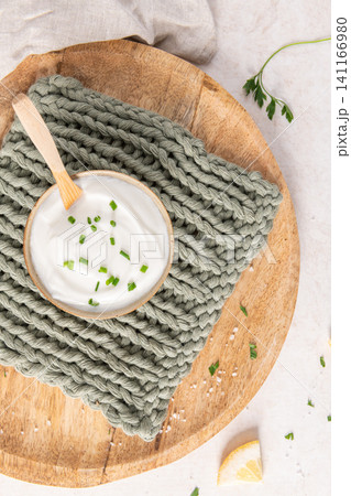 Creamy yogurt dip in a rustic bowl garnished with fresh green chives on a wooden board with a soft knit texture backdrop for a healthy snack Creamy yogurt dip in a rustic bowl garnished with fresh green chives on a wooden board with a soft knit texture backdrop for a healthy snack 141166980
